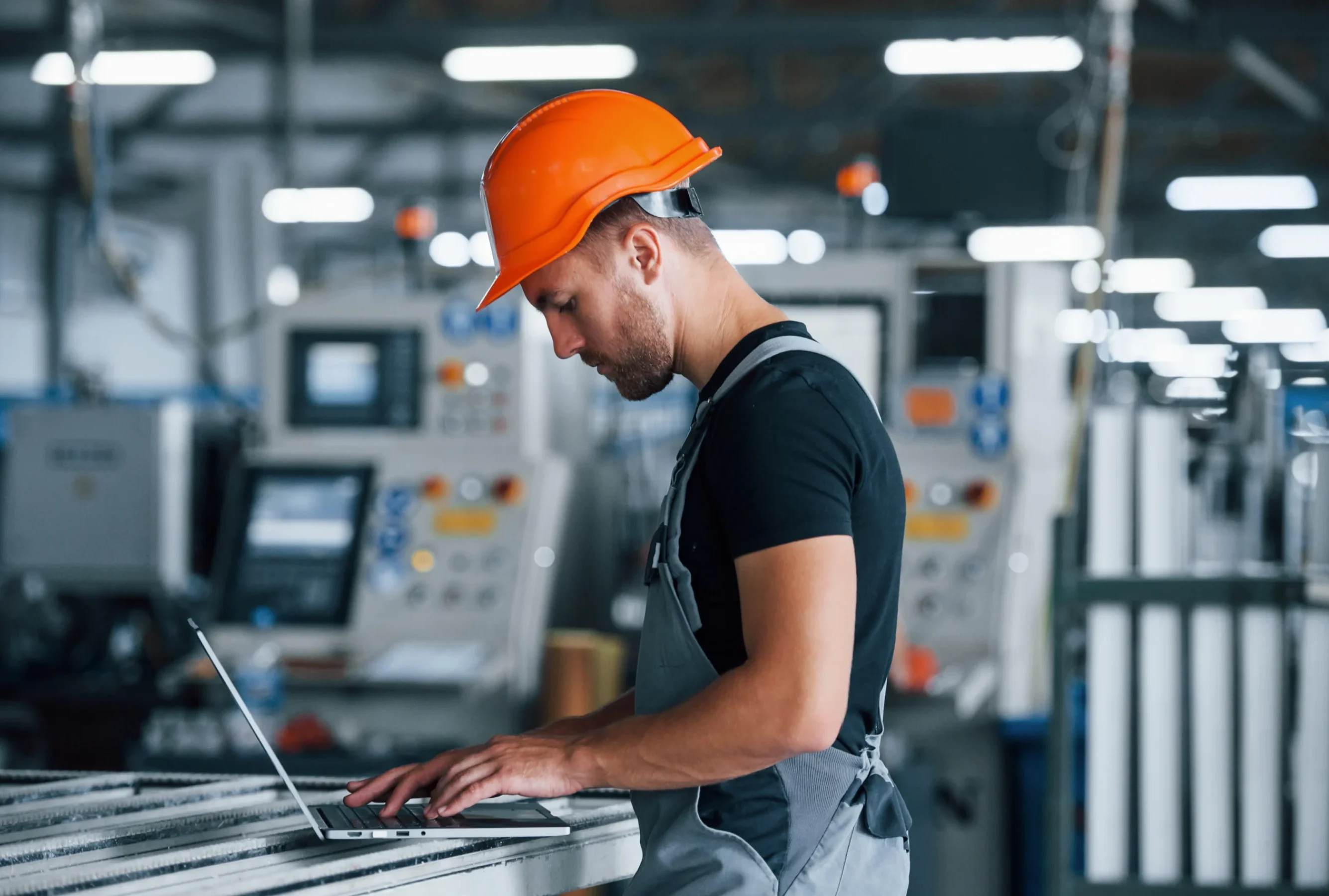 Industrial worker wearing a safety helmet using a laptop inside a manufacturing facility for manufacturing web development and digital operations.